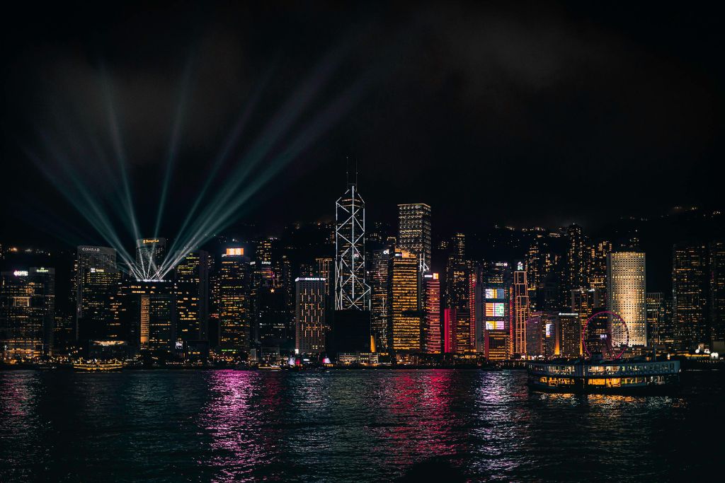 Night view of Hong Kong’s Victoria Harbour with neon-lit skyscrapers and laser beams streaming into the sky during the Symphony of Lights. Watching this nightly show is one of the best things to do in Hong Kong at night and a highlight of many Hong Kong attractions.