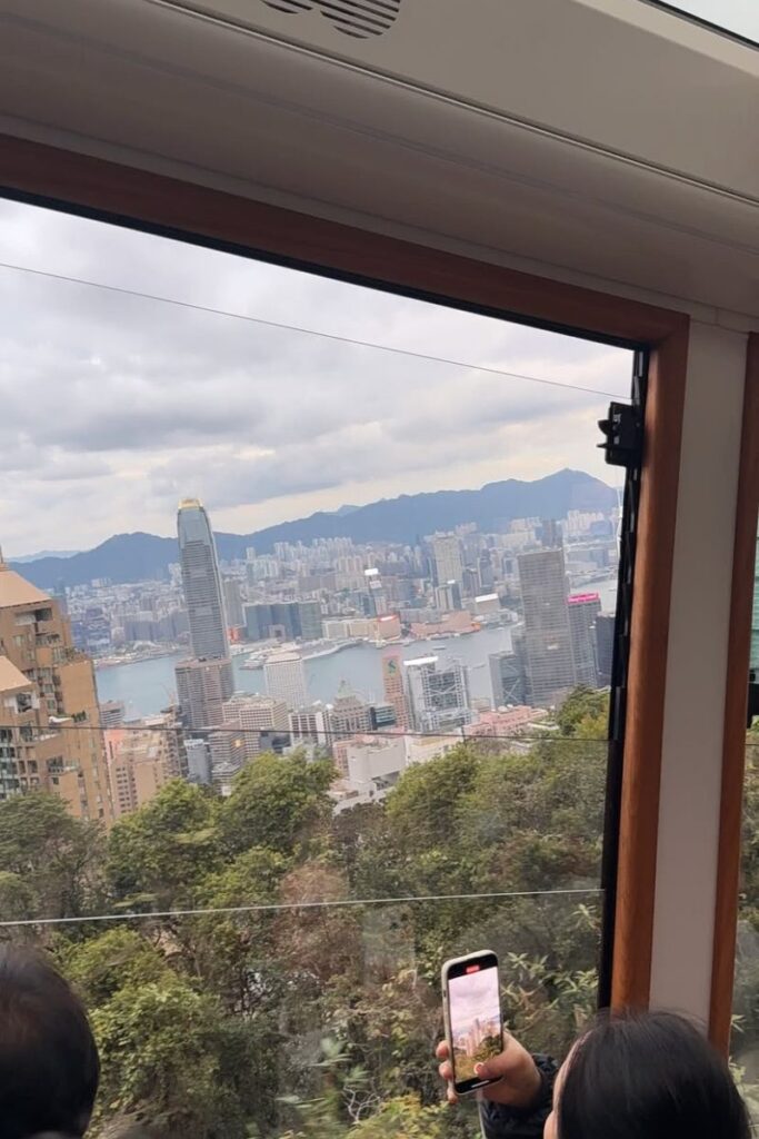 Passenger captures a photo of the Hong Kong skyline through the window of the Peak Tram as it climbs Victoria Peak. One of the best things to do in Hong Kong China, the ride offers spectacular views and fits well into any Hong Kong itinerary.