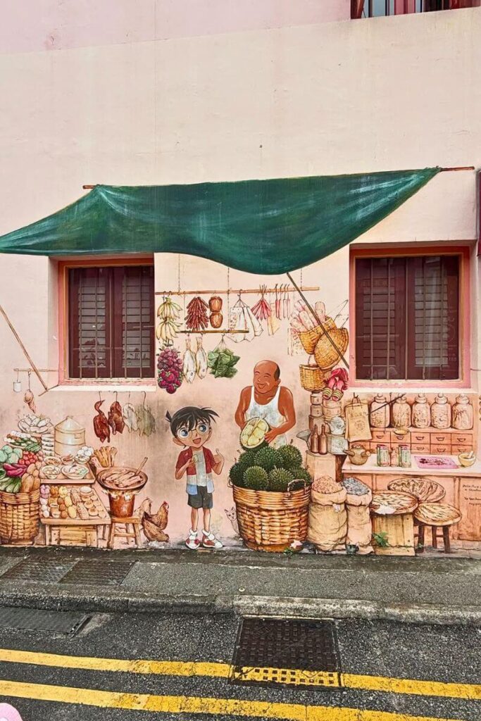 Whimsical mural painted on a pink wall shows an old-school Singapore market scene with a cheerful vendor, baskets of durians, and a cartoon child. This creative artwork is one of the hidden gems in Singapore and a fun way to explore its street art and heritage.