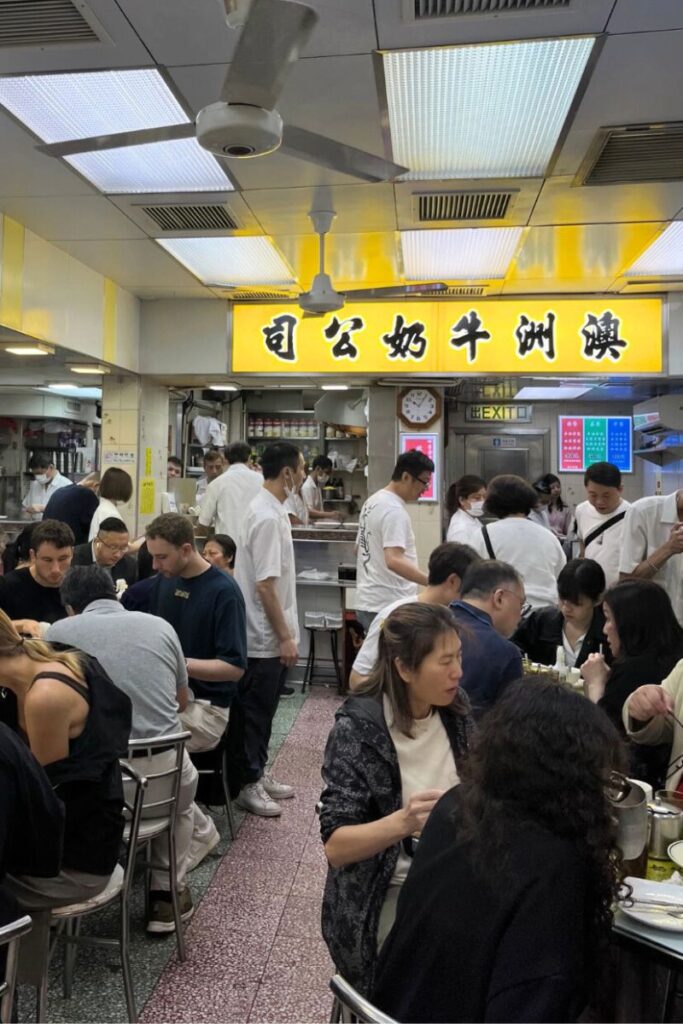 A crowded Hong Kong cha chaan teng with locals and tourists enjoying casual Cantonese food under a bright yellow sign. Dining at local eateries is one of the top Hong Kong tips and tricks for authentic food.