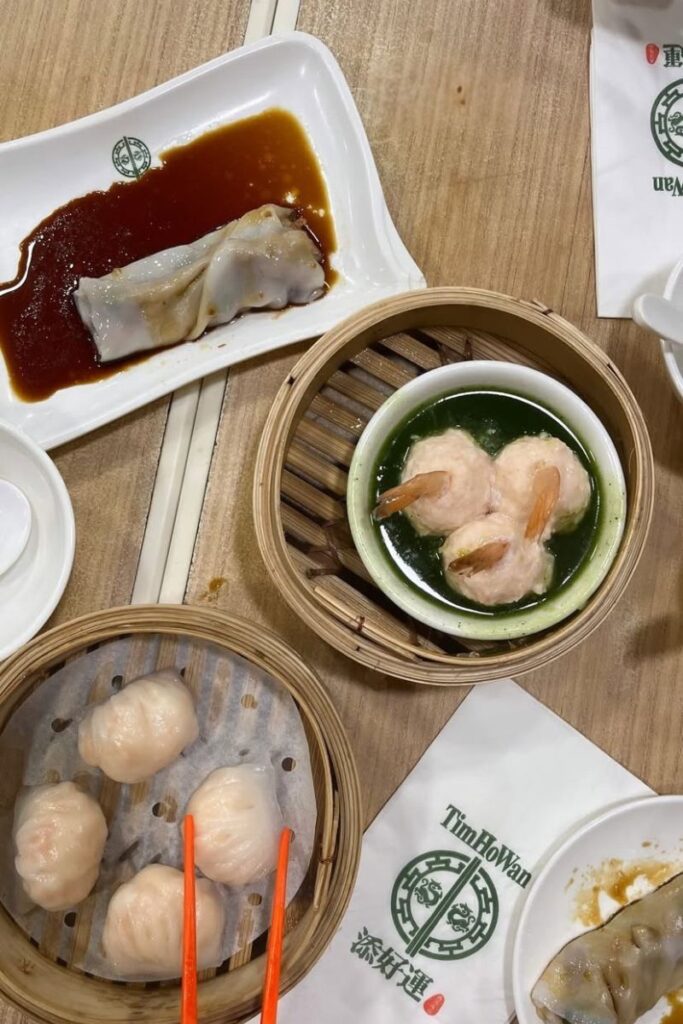 Steaming baskets of har gow dumplings, shrimp balls, and rice noodle rolls at Tim Ho Wan dim sum restaurant. Trying dim sum is one of the most essential things to know before visiting Hong Kong.