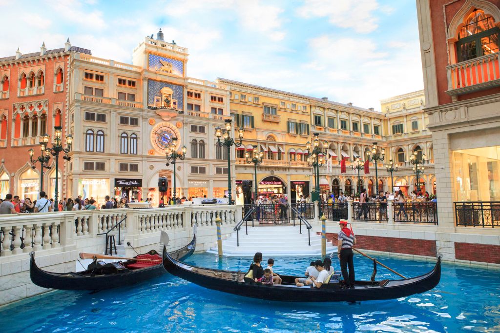 Tourists ride gondolas on the indoor canals of The Venetian Macao resort with Italian-inspired architecture and shops. A common Hong Kong travel tip is to take a day trip to Macau for unique attractions.