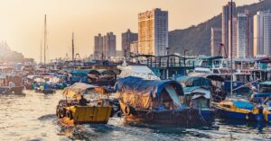 Traditional wooden fishing boats and sampans float in the harbor at sunset with high-rises in the background. Exploring fishing villages is one of the best travel tips for Hong Kong and often recommended in guides with tips for visiting Hong Kong.