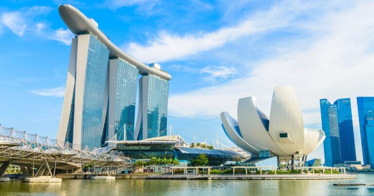A bright daytime view of Marina Bay Sands and the lotus-shaped ArtScience Museum beside the Helix Bridge, all reflected in the calm waters of Marina Bay. These futuristic Singapore landmarks are top highlights for anyone researching what to do in Singapore and are must-sees for travelers exploring unique things to do in Singapore.