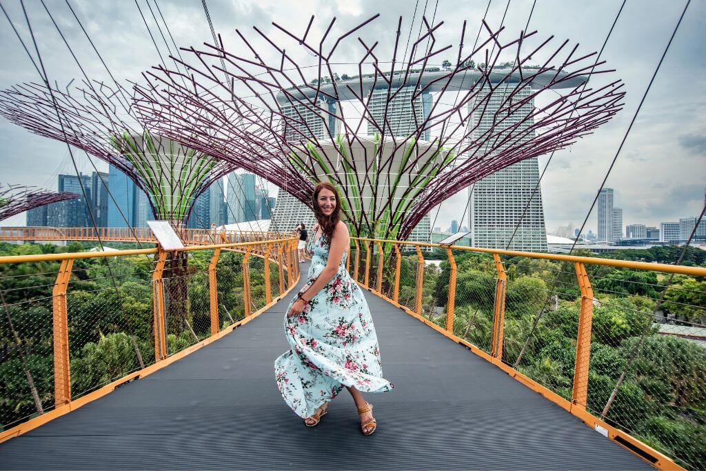 A woman in a floral dress twirls on the OCBC Skyway at Gardens by the Bay, framed by towering Supertrees and the iconic Marina Bay Sands in the background. This scenic walkway is one of the most Instagrammable things to do in Singapore and a must-visit for nature and architecture lovers.