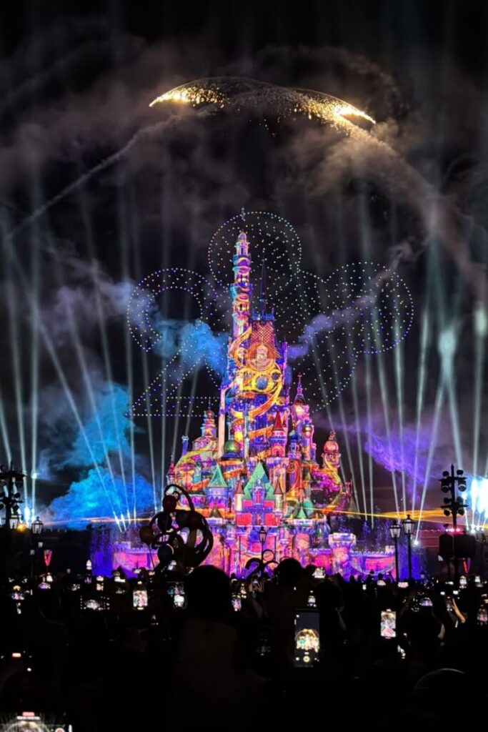 Crowds gather in front of the illuminated Disney castle at night during a vibrant fireworks and laser show at Hong Kong Disneyland. The nighttime spectacular is one of the most magical things to do in Hong Kong at night and a highlight of any family Hong Kong itinerary.