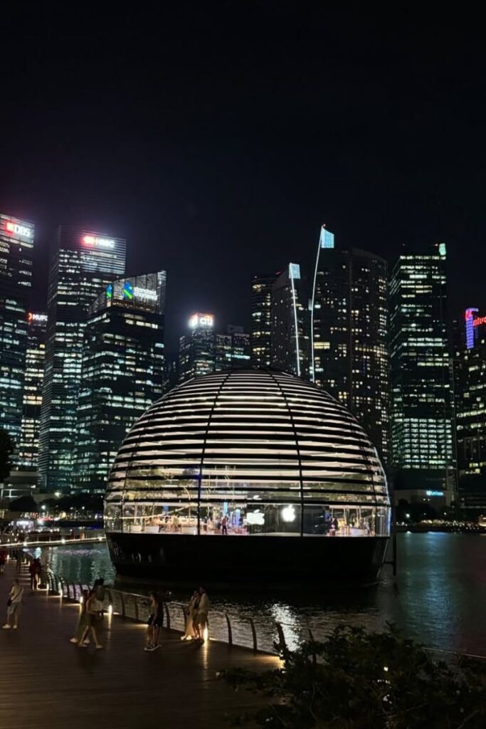 The glowing orb-shaped Apple Store at Marina Bay Sands floats on the water, illuminated against Singapore’s glittering skyline at night. Visiting this unique waterfront retail space is one of the coolest free things to do in Singapore after dark.