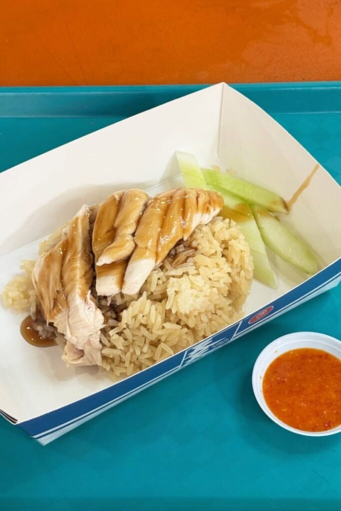 A simple serving of Hainanese chicken rice with chili sauce on the side at a hawker centre. A quintessential dish for food lovers choosing between Singapore vs Hong Kong cuisine.