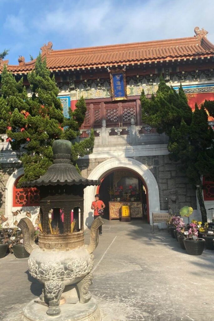 Entrance of Po Lin Monastery with red doors, intricate carvings, and incense burners. This temple near the Big Buddha Hong Kong is an important cultural stop for anyone visiting the Buddha in HK.