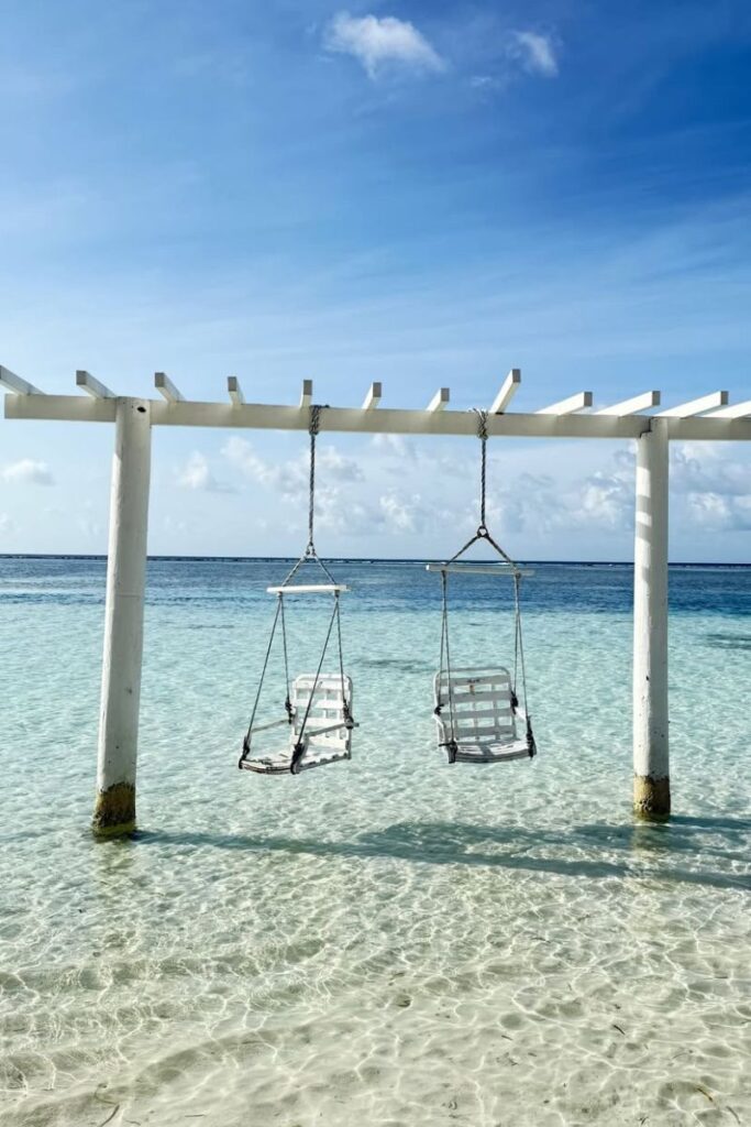 Two wooden swings hang over crystal-clear turquoise water beneath a bright blue sky, a serene escape for anyone seeking warm beaches in December and relaxing winter vacations.