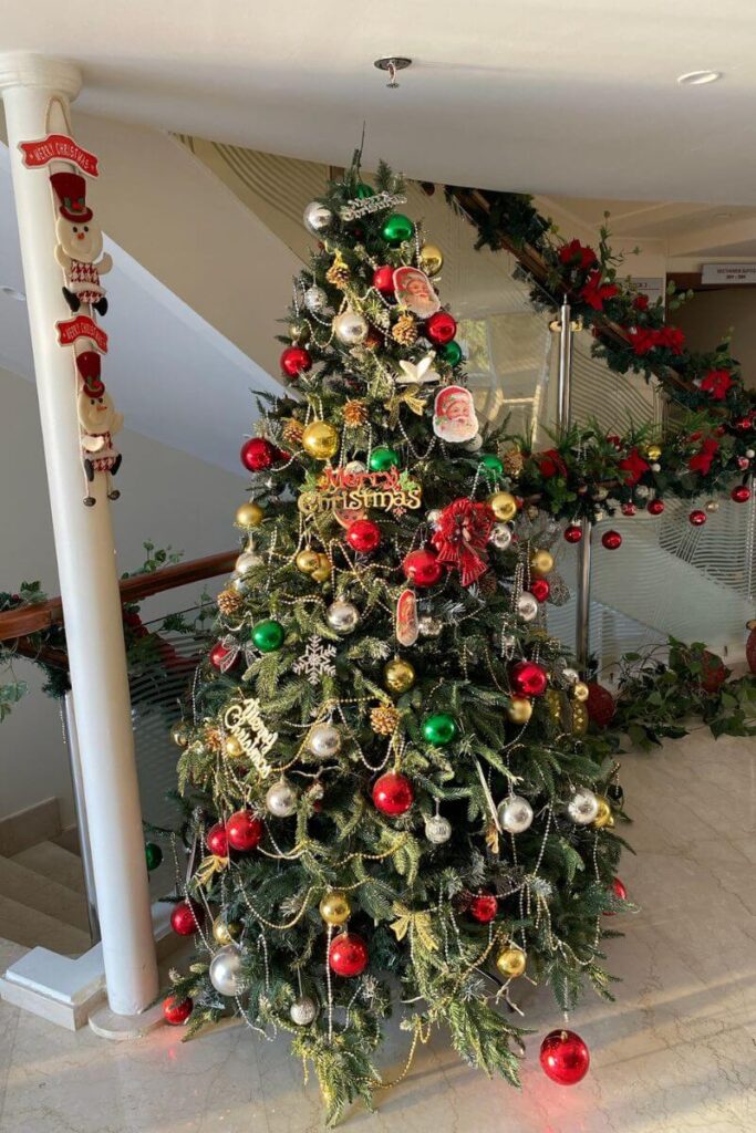 A festive Christmas tree adorned with red, green, and gold ornaments glows under soft light, capturing the spirit of winter vacations spent in warm places during December.