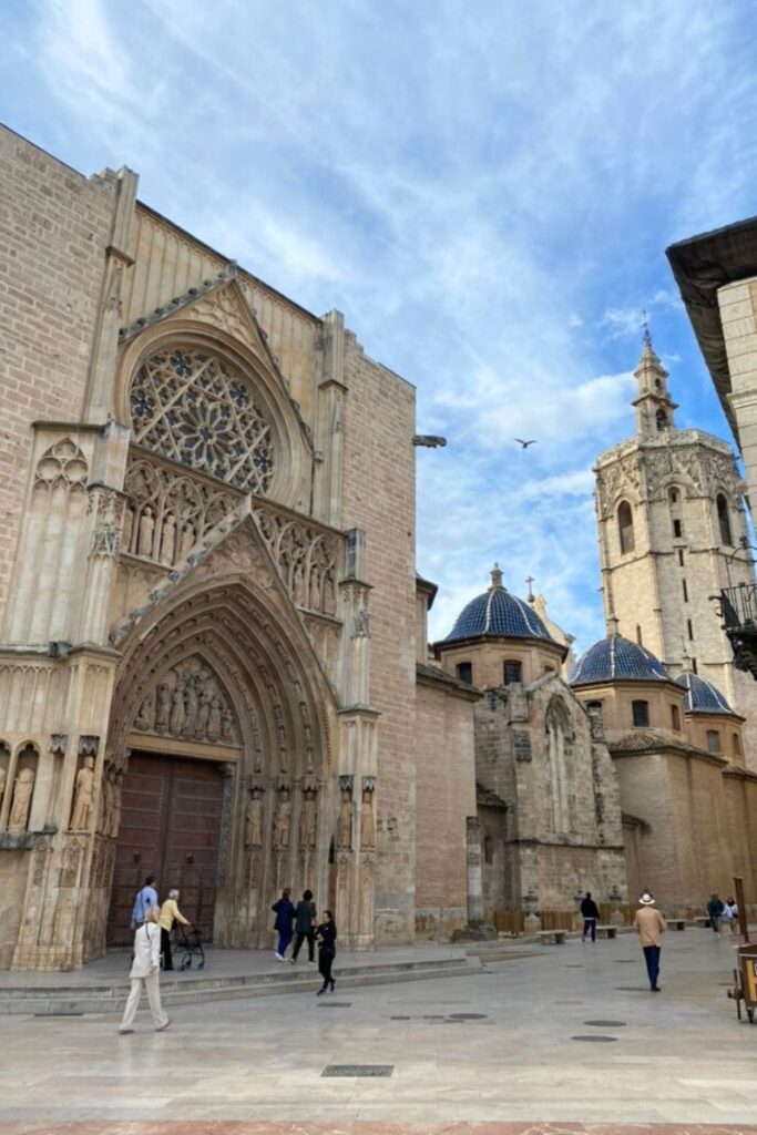 Visitors stroll past a grand cathedral with intricate stone carvings and blue-tiled domes under a bright sky, showcasing one of the best warm European destinations in December for culture lovers.