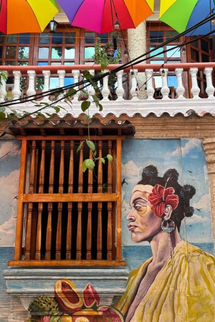 A vibrant street mural featuring a woman with a red hibiscus flower in her hair under rainbow umbrellas in a sunny colonial town. This lively scene is ideal for travelers seeking warm places to visit in December and unique winter getaways in hot countries.