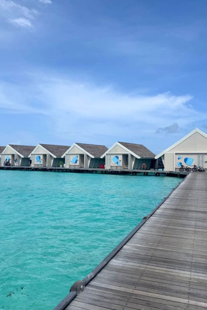 Modern white villas stretch along a wooden boardwalk over turquoise water, offering the ultimate warm place to travel in December and a dream winter vacation escape.