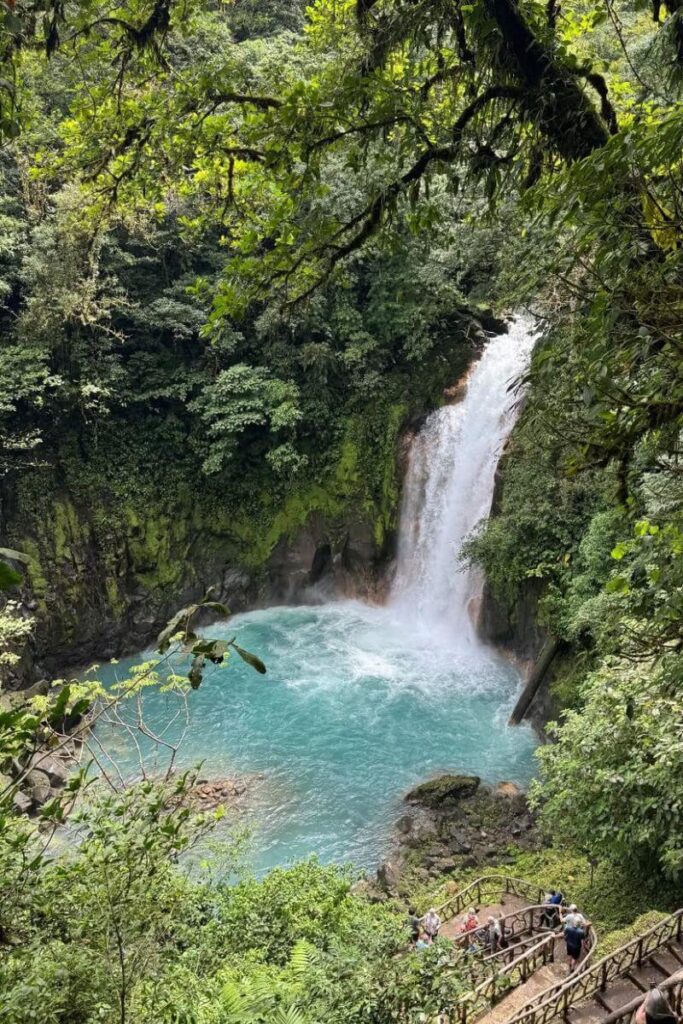 A turquoise waterfall cascades into a lush tropical pool surrounded by dense greenery, highlighting one of the best warm destinations in December for nature adventures.