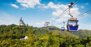 The Ngong Ping 360 cable cars glide above green hills with the Hong Kong Big Buddha statue on the horizon. An iconic experience on a Lantau Island itinerary.