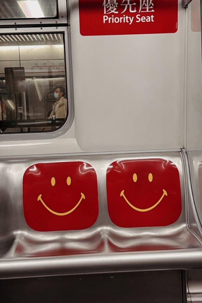 Inside view of a Hong Kong MTR train with red seats marked by yellow smiley faces and a “Priority Seat” sign. Taking the MTR is one of the easiest ways to start a trip to the Big Buddha Hong Kong.