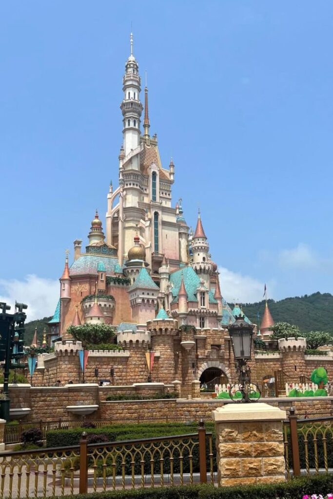 The majestic Hong Kong Disneyland Castle rises against a clear blue sky, featuring colorful spires and intricate details. An iconic attraction and one of the top things to know before visiting Hong Kong for families.