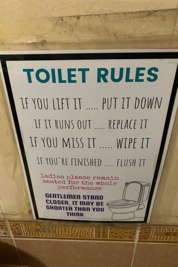 A funny sign in a shared hostel bathroom titled “Toilet Rules,” reminding guests to replace supplies and flush after use. This highlights key hostel shower etiquette and shared bathroom expectations for travelers new to hostel life.