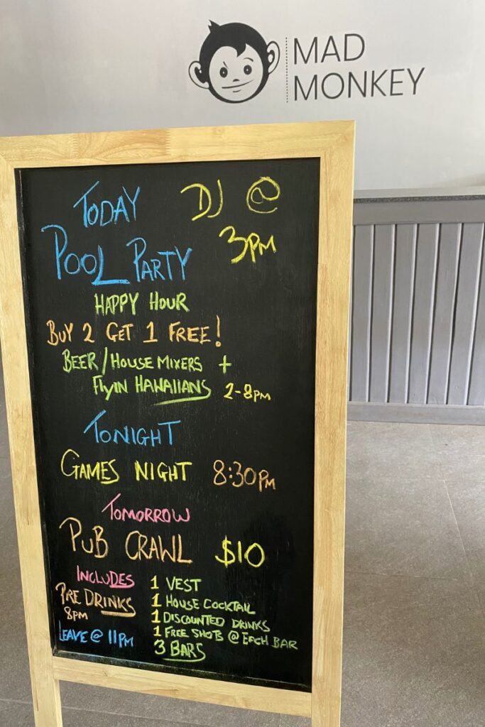 A chalkboard at Mad Monkey Hostel advertises a pool party, games night, and pub crawl with colorful writing. It showcases the lively hostel standards of social events and a great way to meet hostel friends while traveling.