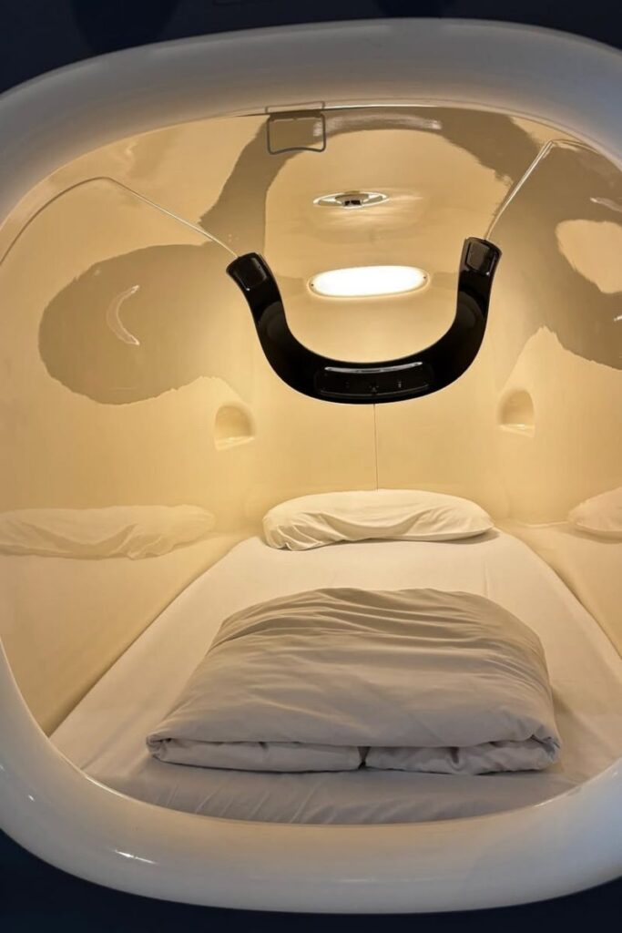 A modern capsule-style hostel bed with soft white bedding and a sleek light overhead. This cozy sleeping pod illustrates hostel bedding quality and what to expect when sleeping in a hostel with private pods.