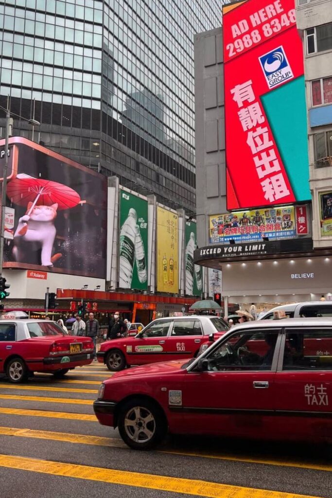 Red taxis and bright billboards light up a bustling Hong Kong street scene. This lively city atmosphere contrasts with the calm at the HK Big Buddha.