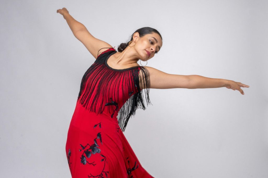 A woman in a red dress poses mid-dance against a plain backdrop, illustrating spending cuts on hobbies as a way to save money for travel and prioritize travel savings over extras.