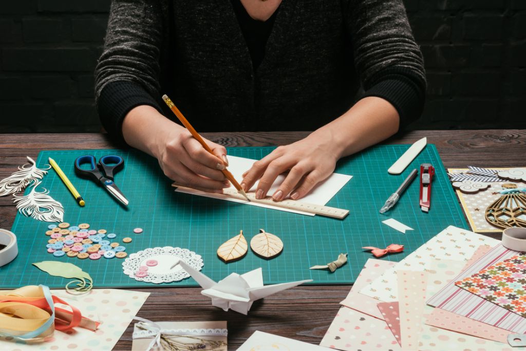 Hands measure paper on a crafting table filled with ribbons, buttons, and cutouts, perfect for DIY travel vision board template free printables and creative travel mood board ideas.