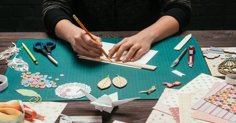 Hands measure paper on a crafting table surrounded by scissors, ribbons, and decor, ideal for creating a travel vision board template or DIY travel dream board printables.