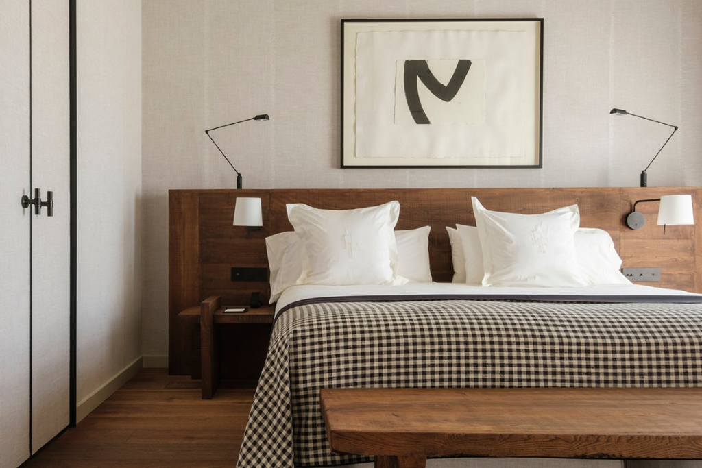 A bright contemporary hotel room features warm wood furnishings, crisp white bedding, and understated artwork above the bed. An inviting example of where to stay in Mallorca Spain for first-time visitors seeking comfort and style.